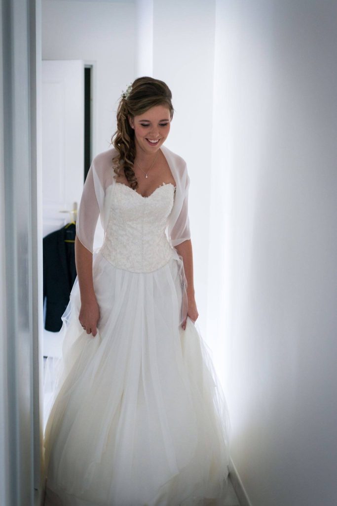 Femme en robe de mariée, souriante, dans un couloir éclairé.