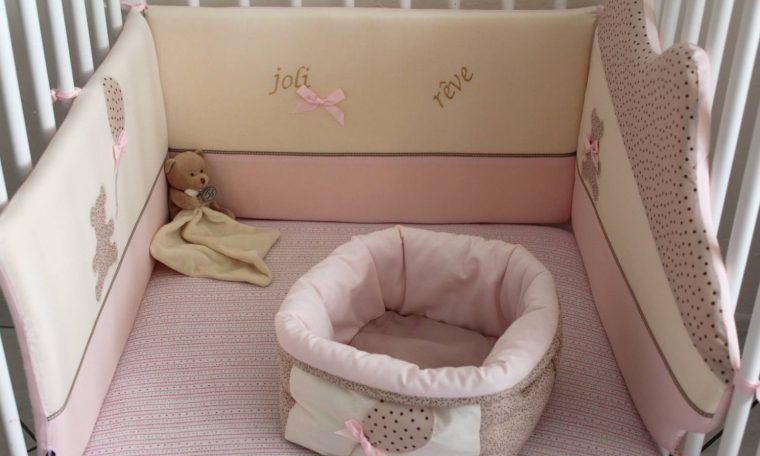 Lit de bébé avec parois rembourrées roses et un coussin en forme de nid.